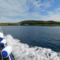 View from the side of a rib style boat travelling across the sea towards an island