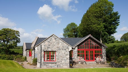 A house with stone walls and large red windows overlooking a garden