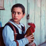 An anxious looking school girl is seated holding a chicken