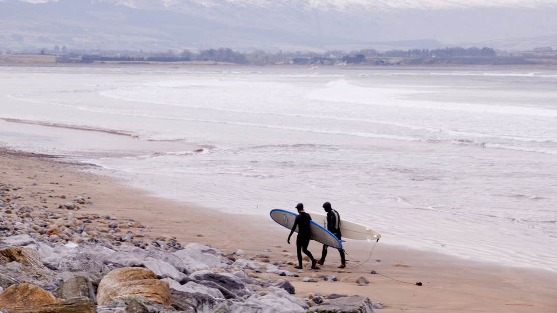 Two surfers walking along Strandhill Beach in Sligo holding their boards
