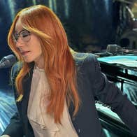 A woman with eyes closed is playing 2 keyboards and singing into a mic.