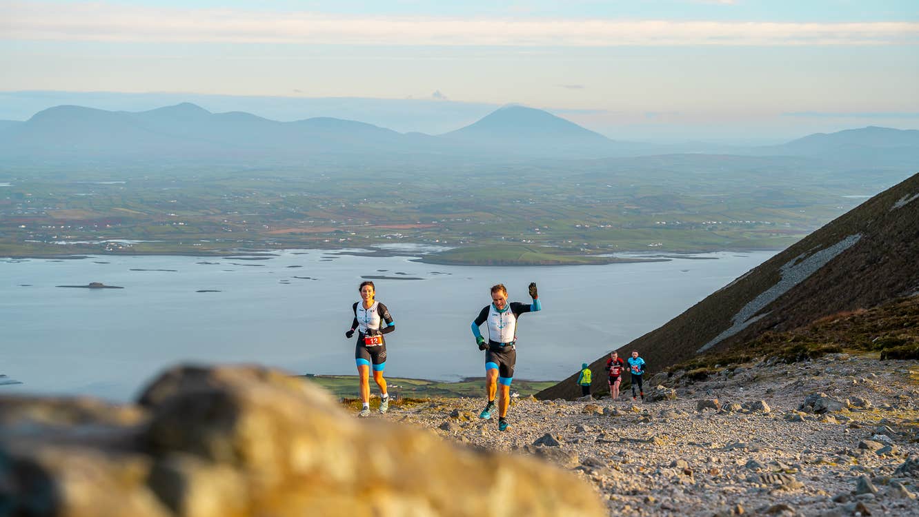 2 runners seen on a small rocky area with views of hills in the background.
