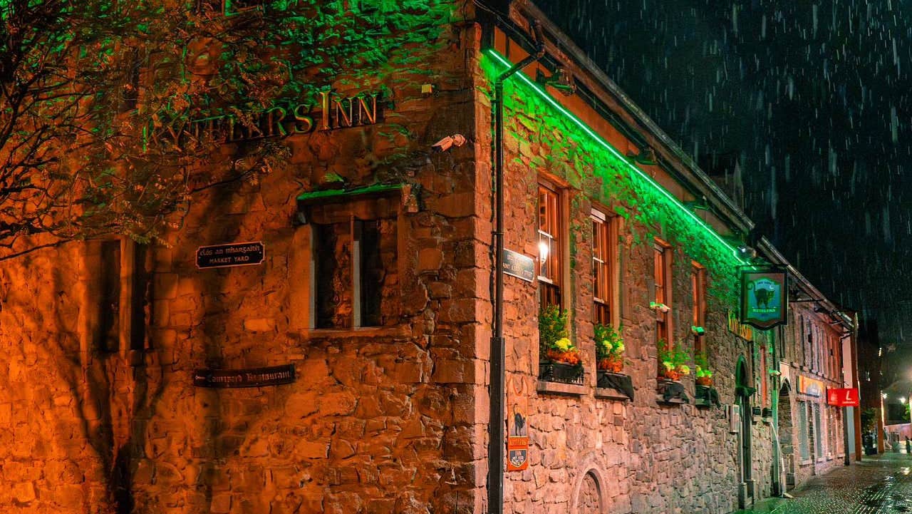 Exterior of a stone pub with green lighting on a rainy night