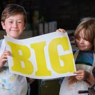 2 smiling young children holding up a large printed piece of paper with single large word on it.