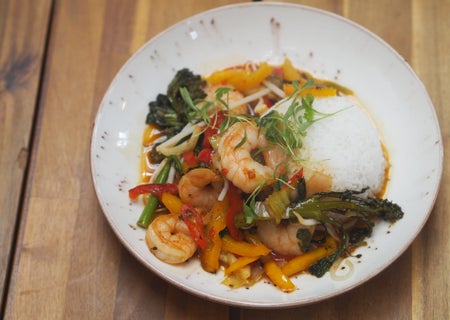 White plate with rice prawns and peppers on a wooden table