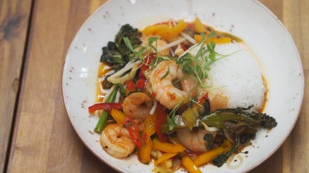 White plate with rice prawns and peppers on a wooden table