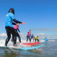 Kids on surf boards taking surfing lessons with an instructor in shallow waters