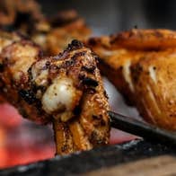 Close up view of meat on skewers cooking over flames.