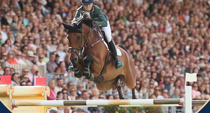 RDS Dublin Horse Show 2026 - a horse and rider in full flight over a jump with large full arena stand in the background.