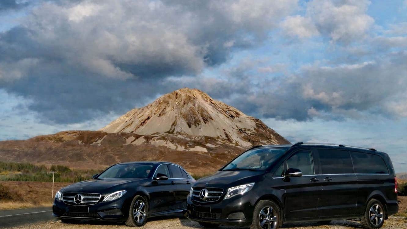 Two black Mercedes vehicles parked in front of a mountain