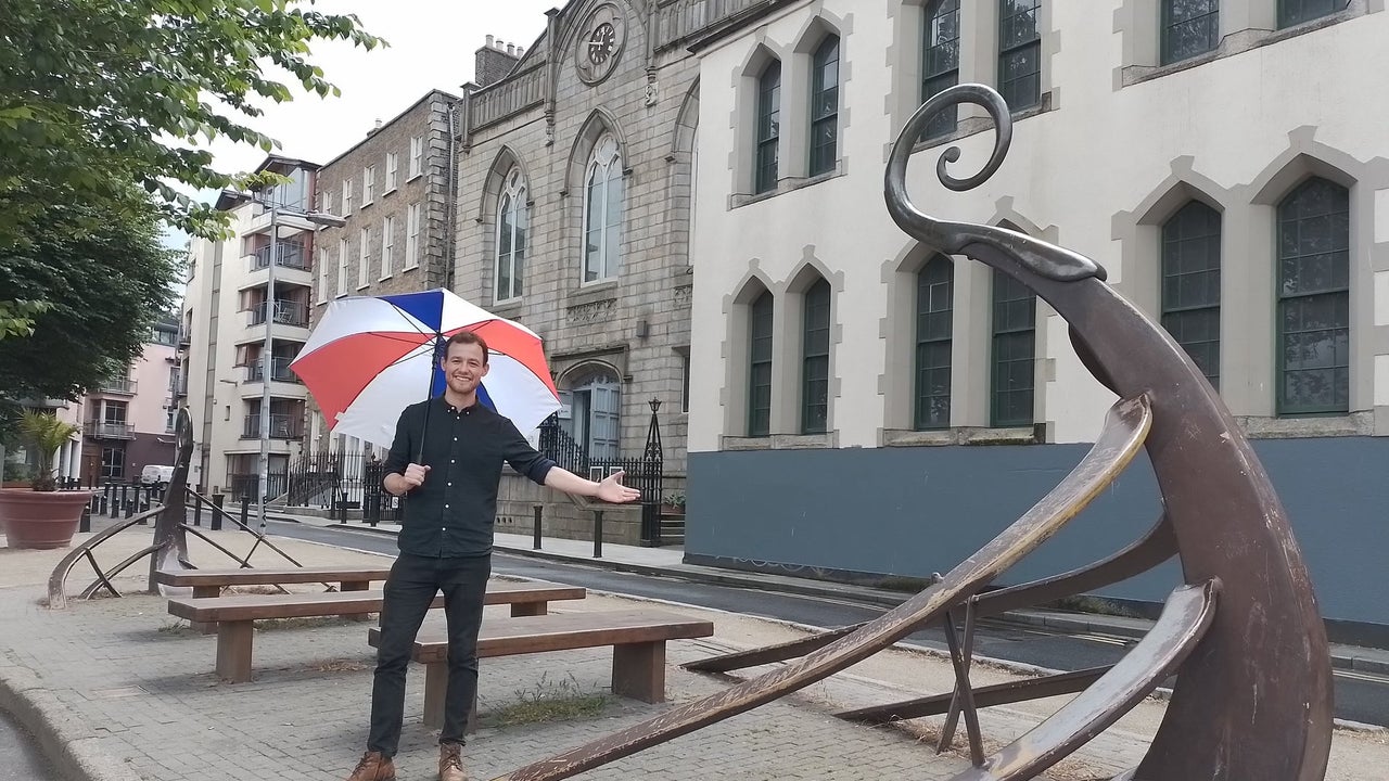Person holding an umbrella standing on a street with wooden seats