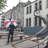 Person holding an umbrella standing on a street with wooden seats
