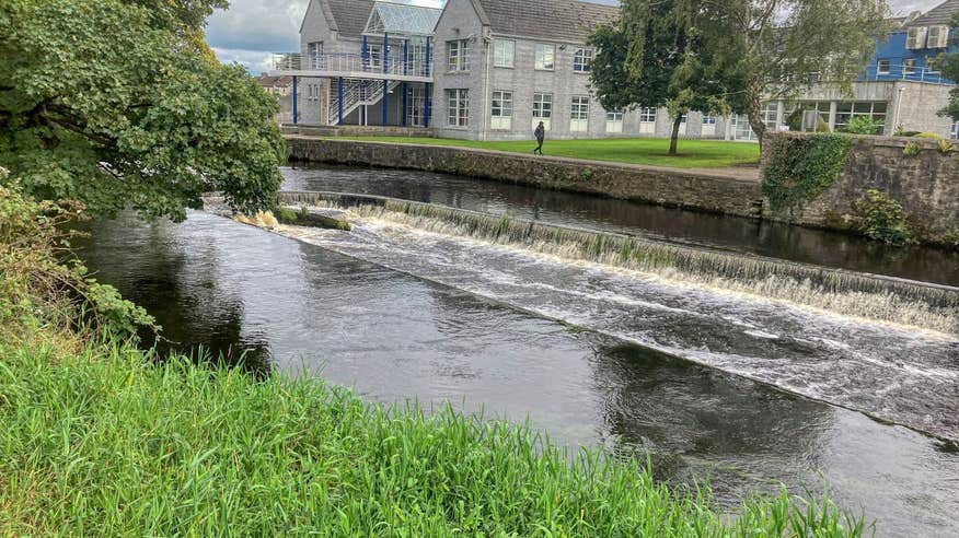 Green riverbanks and buildings along the Mall Walk, Co. Longford