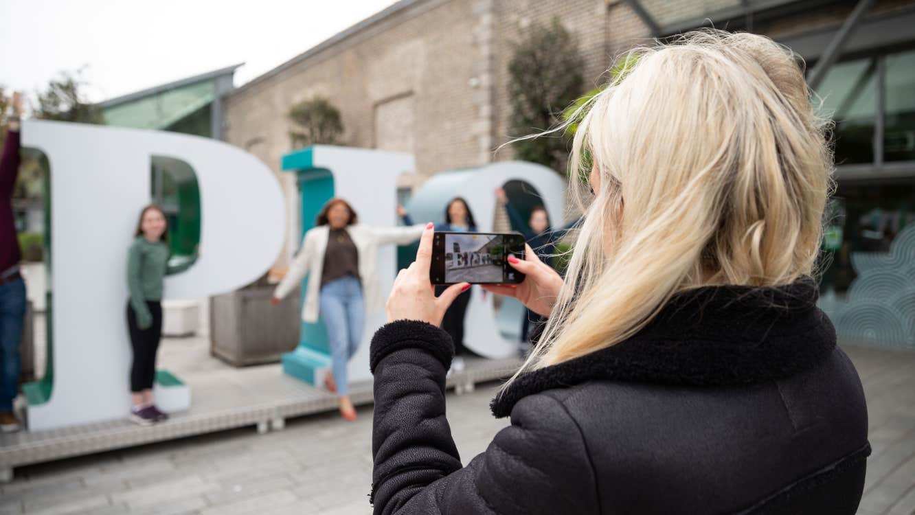 Blonde haired girl holding up a phone to take a photo of her friends at the EPIC sign