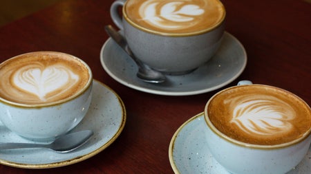 Three cups of coffee on saucers with teaspoons on a table