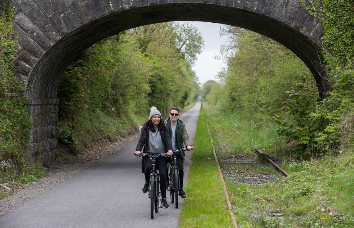 Two people cycling under a stone bridge on a cycle path in Westmeath