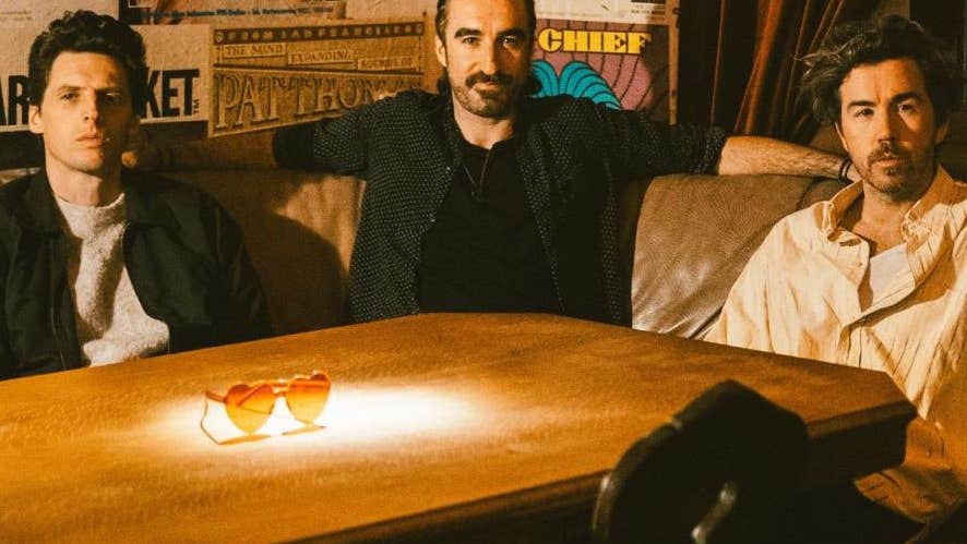 3 men seated around a wooden table on a corner couch