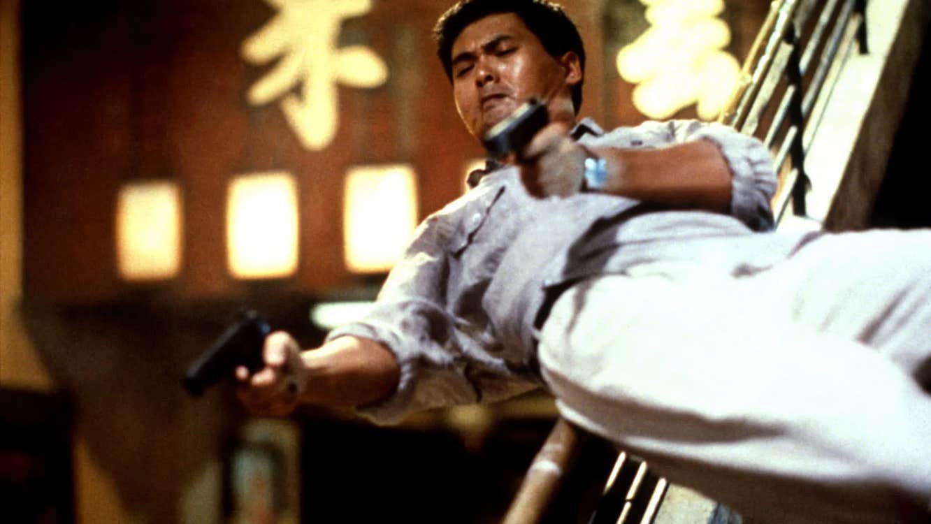 A man sliding down a banister, with a pistol in each hand.