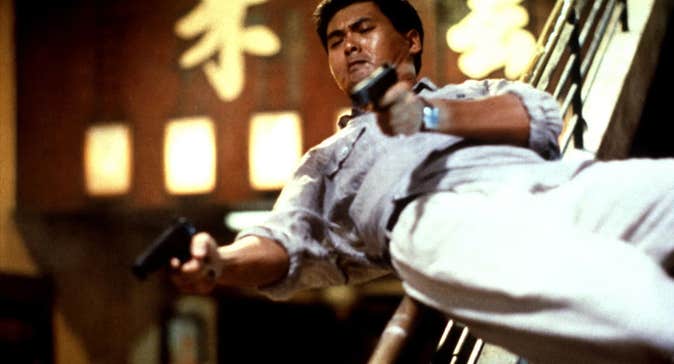 A man sliding down a banister, with a pistol in each hand.