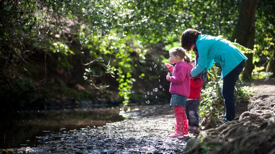 Mother and children blowing bubbles by a river 