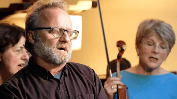 A seated man is singing with his eyes closed