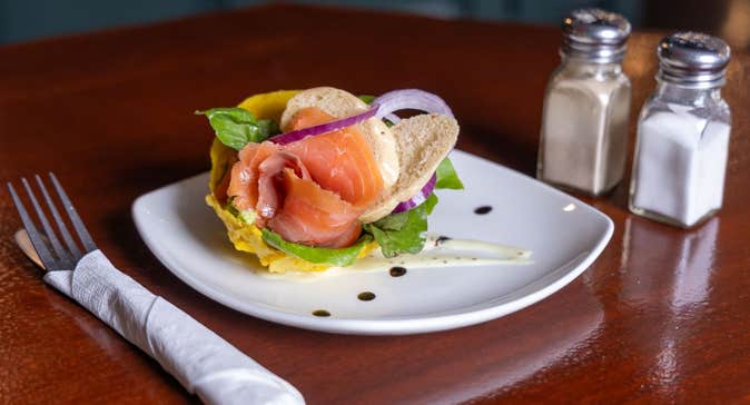 Smoked salmon served with bread and garnishes on a white plate with cutlery and condiments