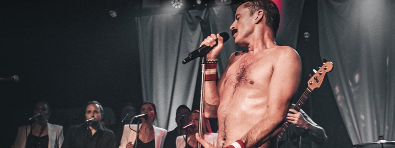 A bare chested man singing with a mic on a stage.
