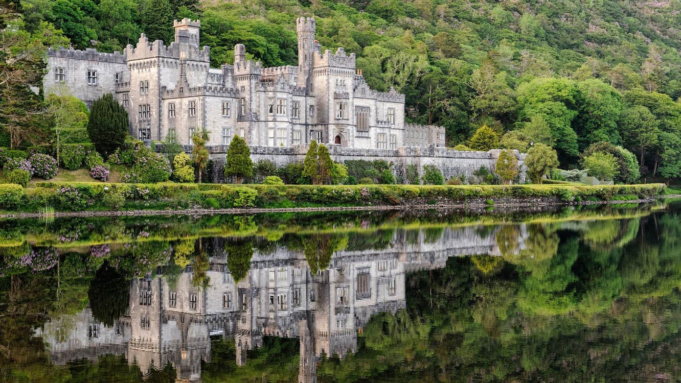 Kylemore Abbey reflected on the surface of a lake with a mountain of shrubs and trees behind it
