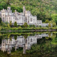 Kylemore Abbey reflected on the surface of a lake with a mountain of shrubs and trees behind it