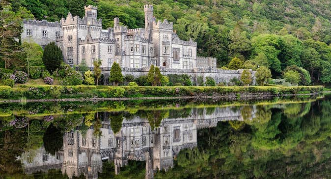 Kylemore Abbey reflected on the surface of a lake with a mountain of shrubs and trees behind it