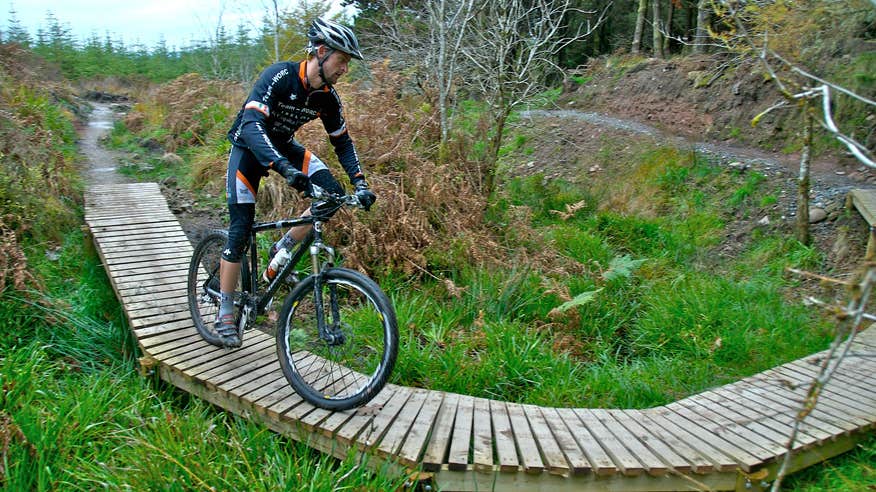 A man wearing biking gear and a helmet cycling on a boardwalk