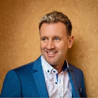 Mike Denver - a smiling man looking away to his right against dark gold background.