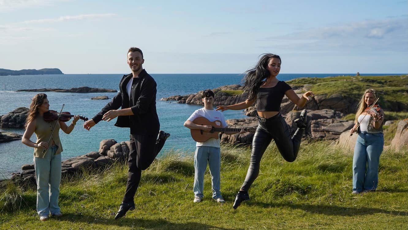 5 people standing with instruments or leaping in the air, outdoors on a rocky edge overlooking the sea.