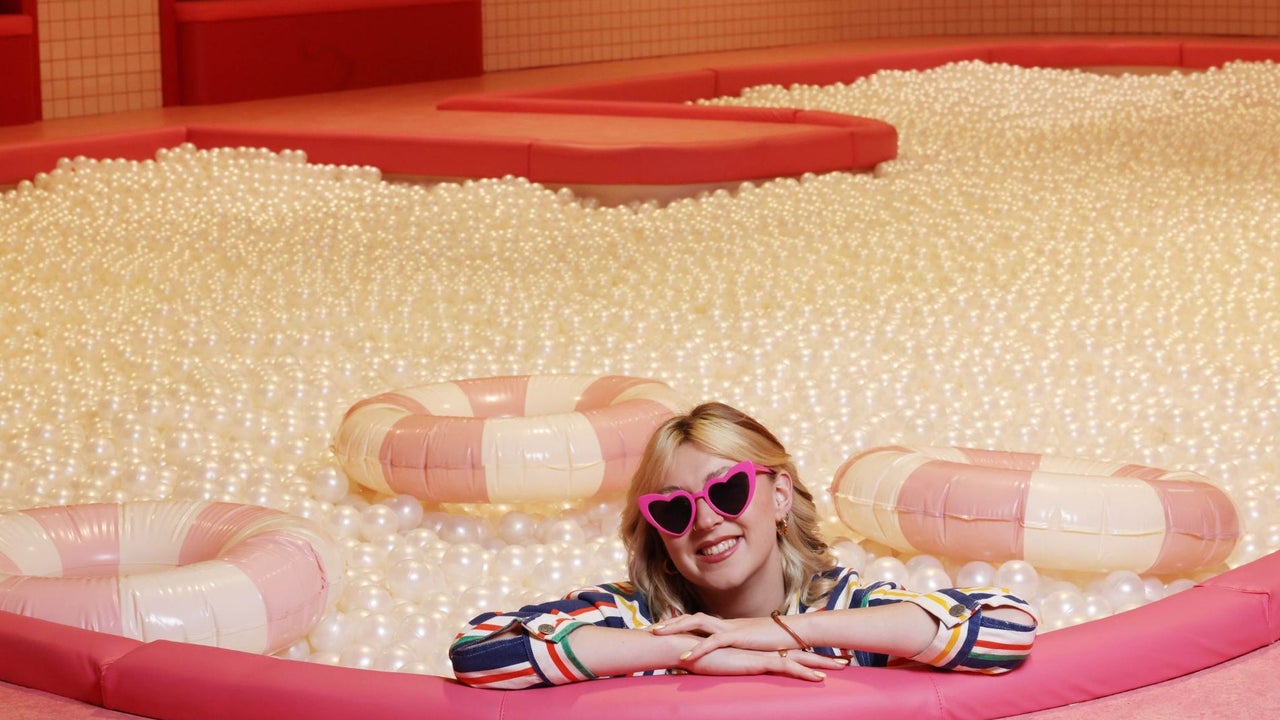 Person wearing pink heart shaped sunglasses in a full ball pit with three inflatable lifebuoys