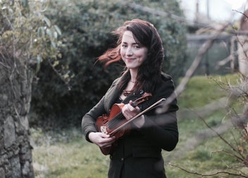 A woman standing beside a tree with a fiddle in her hand