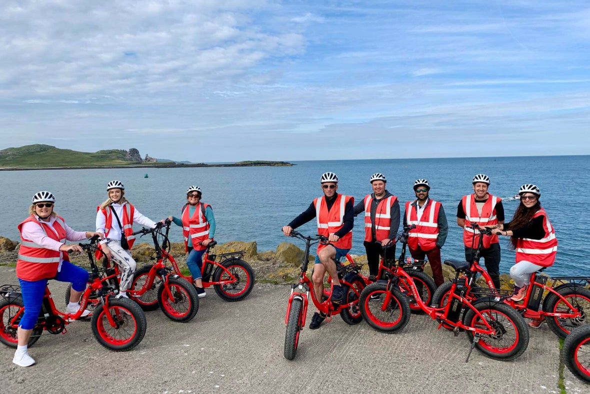 A group of people on a bike tour in Howth, Dublin. Everyone is wearing yellow security vests and helmets with bright orange electric bikes.