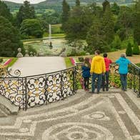 A small tour group standing on a balcony overlooking a decorative garden