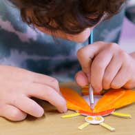 Children's art workshop with Cas McCarthy, a child leaning over a small piece of art work, painting.