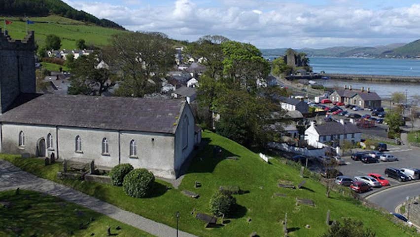 An old church on a small hill overlooking a town with the sea in the distance