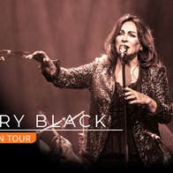 Mary Black The Slán Tour, a woman singing into a mic on a stand with right arm outstretched forward.