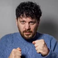 A man in blue knitted jumper holding his hands up in fists.