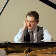 Michael McHale is resting his head on one of his hands as he sits pensively at a piano.