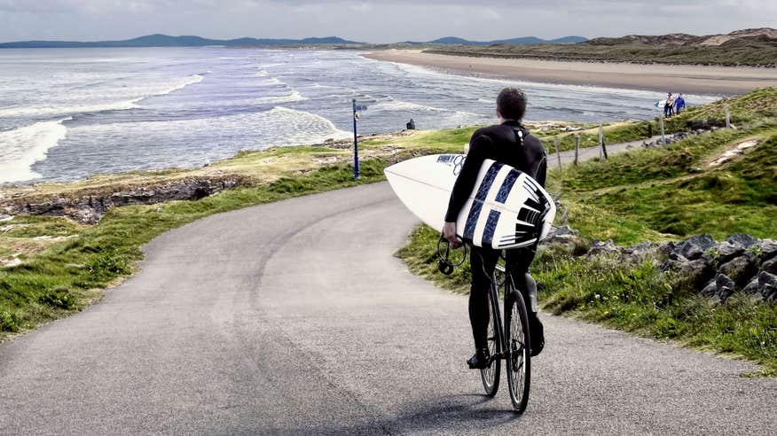 Surfer riding his bike to the beach to go surfing in Bundoran, Donegal