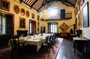 A hall in a period house with wood flooring and a large banquet table prepared for a meal