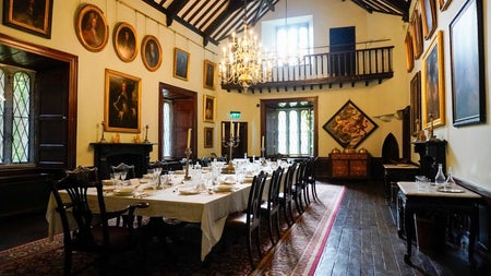 A hall in a period house with wood flooring and a large banquet table prepared for a meal