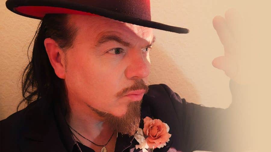 Close up view of man wearing a hat, holding up one hand as if to protect from bright light.