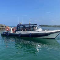 A passenger boat cruising on calm blue water with rocky shoreline and green hills in the background