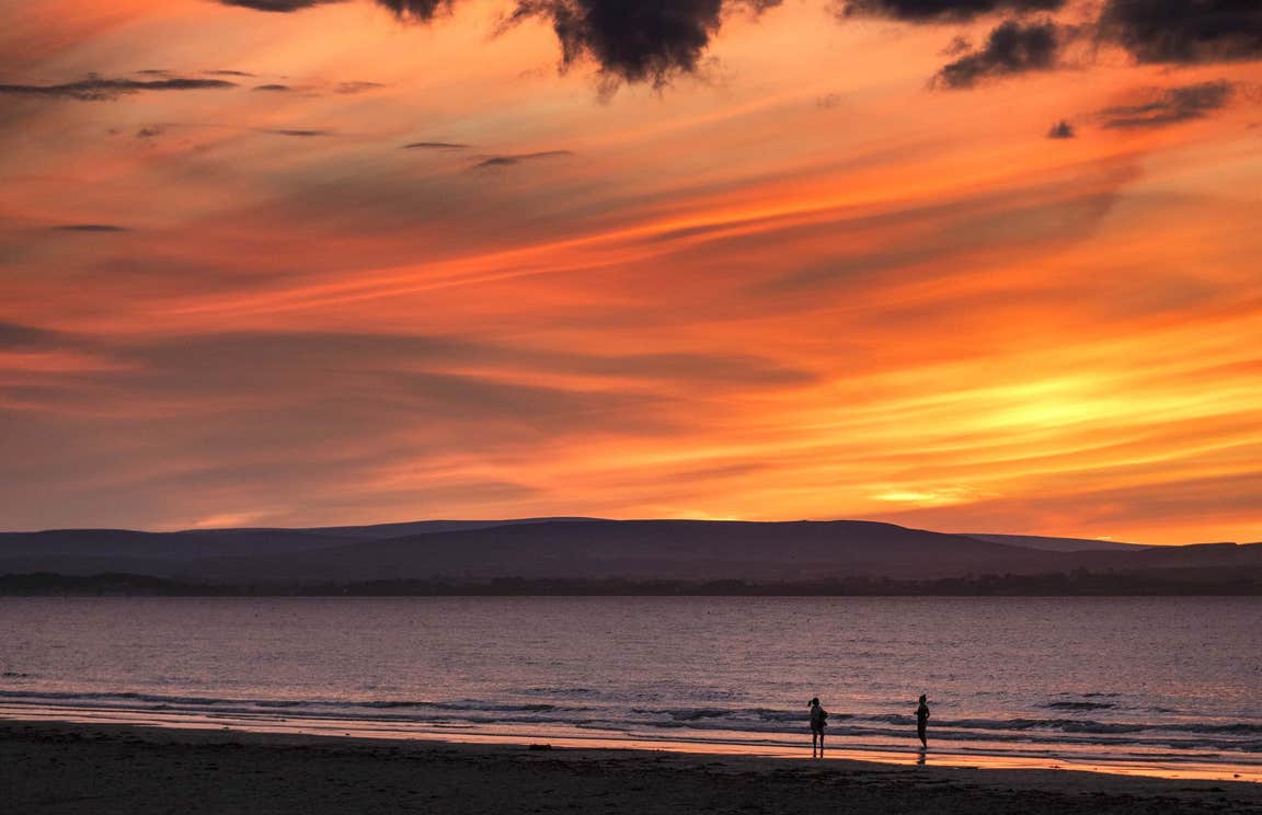 Two people walking on Enniscrone Beach in County Sligo at sunset.