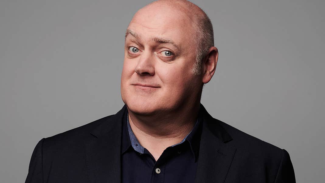 A man with quizzical smile in dark shirt and jacket.