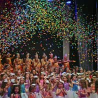 A large group of children gathered on a stage with confetti falling from above